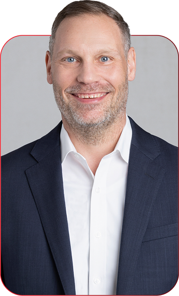 Smiling middle-aged man in a navy suit and white shirt, portrait against a light gray background.